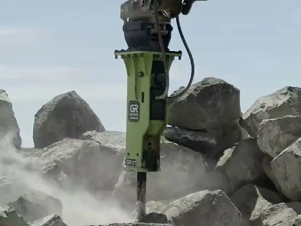 A hi-vis green GoodRock hydraulic breaker driving its chisel into a boulder, throwing rock dust